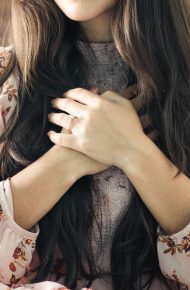 Una ragazza seduta sul letto si tiene le mani al cuore